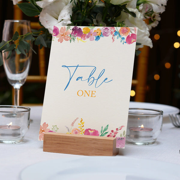 Table number card with floral design on a table setting with candles and glasses.