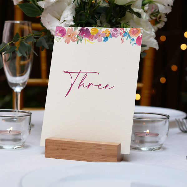 Table setting with a floral table number card labeled 'Three' on a white tablecloth.