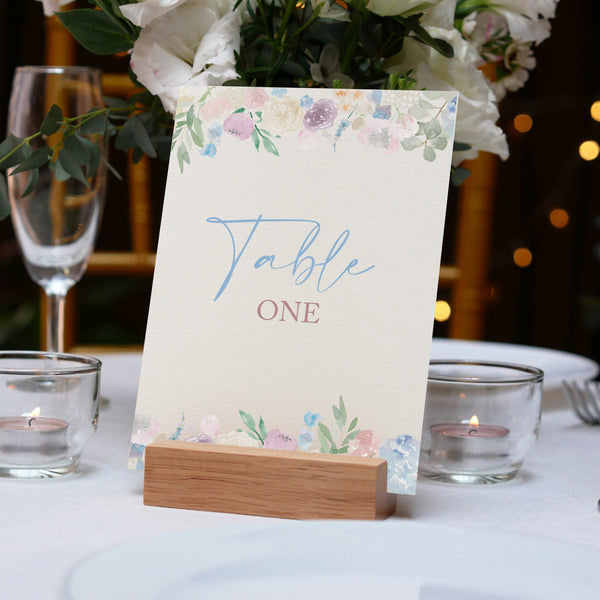 Table number card on a wooden stand with floral design, placed on a table setting with candles and glasses.